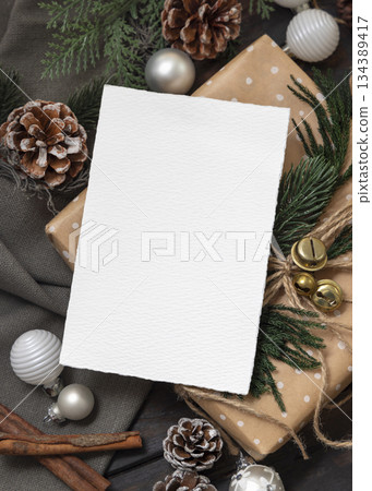 Card on wrapper Christmas present near pine cones, spices and fir twigs, top view. Holiday mockup Card on wrapper Christmas present near pine cones, spices and fir twigs, top view. Holiday mockup 134389417