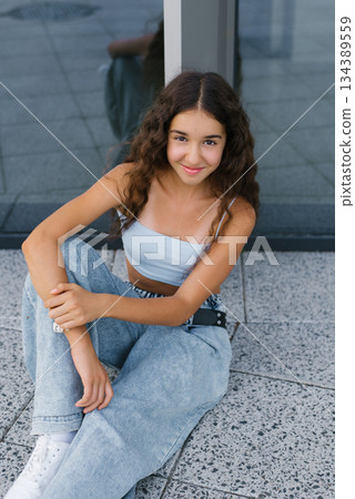 Happy Teen Sitting By Glass Wall Happy Teen Sitting By Glass Wall 134389559