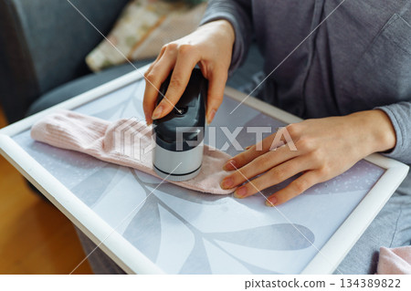 woman takes care of clothes at home, cuts off lint with tool 134389822