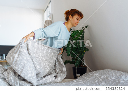 young woman makes bed and folds blanket neatly young woman makes bed and folds blanket neatly 134389824
