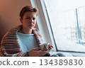 young woman warms up with hot tea in winter weather at home 134389830