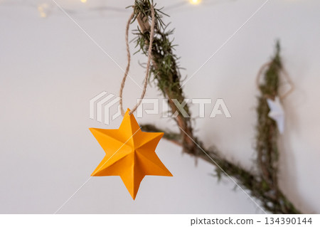 Handmade New Year toy on the branch of a Christmas tree. Yellow star ornament made of paper for a Christmas mood Handmade New Year toy on the branch of a Christmas tree. Yellow star ornament made of paper for a Christmas mood 134390144