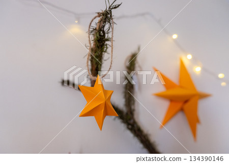 Handmade New Year toy on the branch of a Christmas tree. Yellow star ornament made of paper for a Christmas mood Handmade New Year toy on the branch of a Christmas tree. Yellow star ornament made of paper for a Christmas mood 134390146