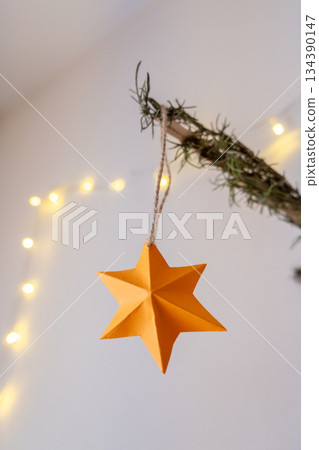 Handmade New Year toy on the branch of a Christmas tree. Yellow star ornament made of paper for a Christmas mood Handmade New Year toy on the branch of a Christmas tree. Yellow star ornament made of paper for a Christmas mood 134390147