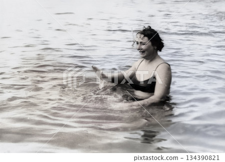 A vintage portrait of middle-aged woman on the seashore. The woman enjoys the cool sea water. Retro photo from 1971. 134390821