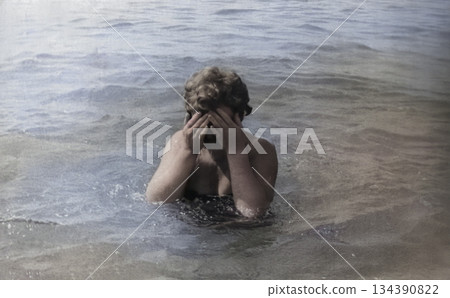 A vintage portrait of a middle-aged woman on the seashore. The woman washes her face with cool seawater. Retro photo from 1971. A vintage portrait of a middle-aged woman on the seashore. The woman washes her face with cool seawater. Retro photo from 1971. 134390822