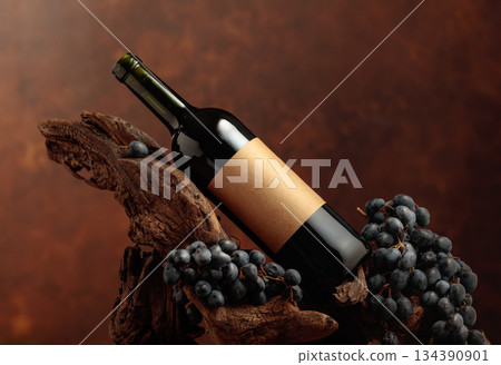 Unopened bottle of red wine, blue grapes, and old snag. 134390901