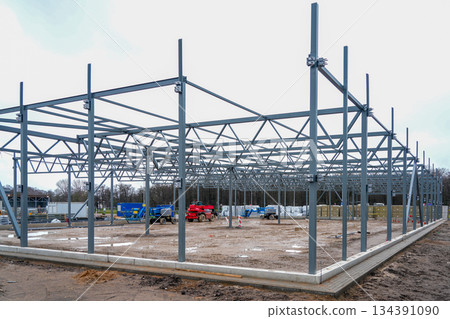 Steel warehouse frame under construction with machinery and materials on industrial building site Steel warehouse frame under construction with machinery and materials on industrial building site 134391090