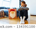 young woman with curly hair sits on floor near bag of Christmas gifts 134391100