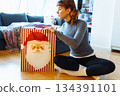 young woman with curly hair sits on floor near bag of Christmas gifts 134391101