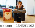 young woman with curly hair sits on floor near bag of Christmas gifts 134391102