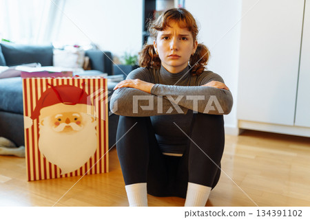 young woman with curly hair sits on floor near bag of Christmas gifts 134391102