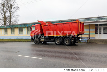 Dump truck sits on the side of the road. Construction equipment is parked near a one-story building. Dump truck sits on the side of the road. Construction equipment is parked near a one-story building. 134391118