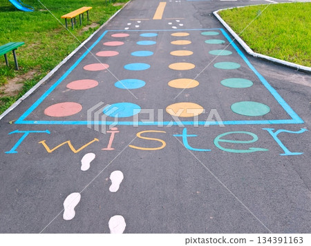 Colorful Twister Game Painted on Outdoor Playground Asphalt. Fun Twister game grid with colored circles and footprints painted on school playground asphalt. Perfect for children activity and recreatio 134391163