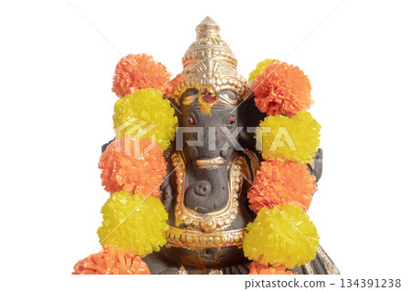 Ganesha idol adorned with a bright orange and yellow floral garland for Hindu worship and celebration. 134391238