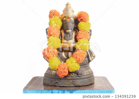 Ganesha idol adorned with a bright orange and yellow floral garland for Hindu worship and celebration. 134391239