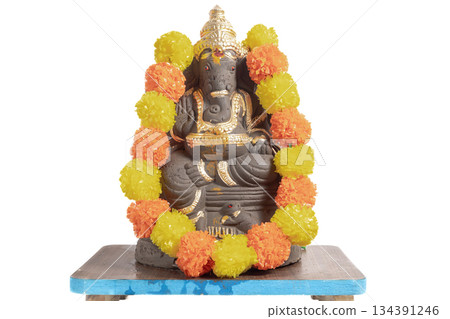 Ganesha idol adorned with a bright orange and yellow floral garland for Hindu worship and celebration. 134391246