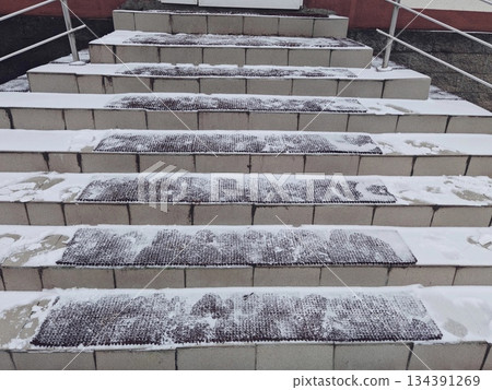 Snow-Covered Concrete Steps with Anti-Slip Mats in Winter. Outdoor concrete staircase lightly covered with snow and equipped with rubber anti-slip mats. Winter urban safety and architecture concept. 134391269