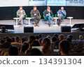 Panel discussion at conference with four speakers on stage and engaged audience in a modern venue 134391304