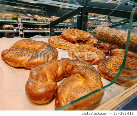 Fresh Baked Bread and Pastries in Bakery Display Case. Assortment of freshly baked bread rolls, pretzels and buns with poppy seeds, sesame and almonds displayed in glass bakery case. Appetizing food p Fresh Baked Bread and Pastries in Bakery Display Case. Assortment of freshly baked bread rolls, pretzels and buns with poppy seeds, sesame and almonds displayed in glass bakery case. Appetizing food p 134391411