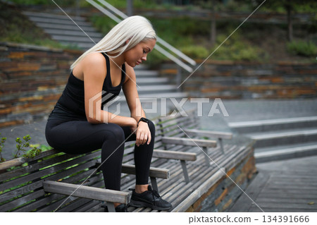 Athletic woman resting on a bench in a serene urban setting 134391666