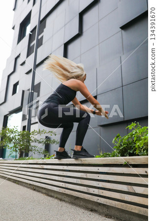 Woman performing exercises during outdoor workout near a modern urban building Woman performing exercises during outdoor workout near a modern urban building 134391670