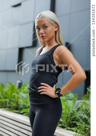 Confident woman in activewear standing outdoors near urban architecture 134391672