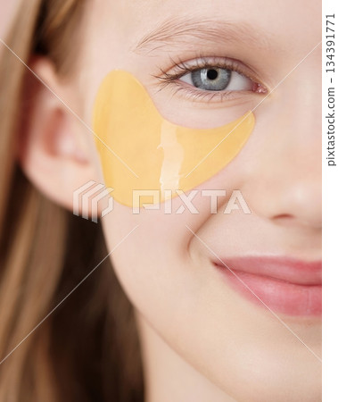 Happy cute young girl with eye patch on studio pink background. Half face portrait of blonde girl gen Alpha smiling looking at the camera. Concept of cosmetics advertisement for teenagers. Adolescent 134391771