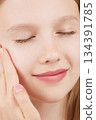 Portrait of smiling cheerful girl doing beauty routine, face massage, applies skin product. Advertisement of self-care products for teenagers. Blonde girl with closed eyes in studio on pink background 134391785