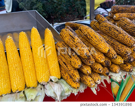Grilled and boiled corn cobs displayed at a street food stall for sale. Local cuisine, outdoor snacking, and traditional street food culture centered around simple seasonal ingredients. Grilled and boiled corn cobs displayed at a street food stall for sale. Local cuisine, outdoor snacking, and traditional street food culture centered around simple seasonal ingredients. 134391898