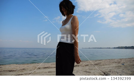 Happy adult woman going on sandy beach near shoreline at sunny day. Beautiful lady walking on seashore with calm waves at background. Concept of summer vacation or holiday. Slow motion Happy adult woman going on sandy beach near shoreline at sunny day. Beautiful lady walking on seashore with calm waves at background. Concept of summer vacation or holiday. Slow motion 134392399