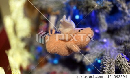 Festive Christmas tree with flying angel pig ornament and blue lights Festive Christmas tree with flying angel pig ornament and blue lights 134392894