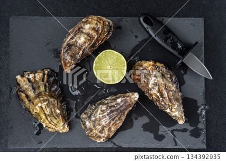 Oysters plate with lemon on black background. Served table with oysters and lemon. Fresh oysters close-up top view. Healthy sea food. Oyster dinner with champagne in restaurant. Oysters with lemon 134392935
