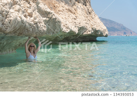 Woman swimming in clear shallow turquoise water beneath a rocky overhang. Bright summer light enhances the tones of the sea and creates a refreshing Mediterranean beach atmosphere ideal for travel and Woman swimming in clear shallow turquoise water beneath a rocky overhang. Bright summer light enhances the tones of the sea and creates a refreshing Mediterranean beach atmosphere ideal for travel and 134393053
