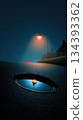 Flickering Street Light Illuminates a Quiet Suburban Street at Night With Reflective Puddle 134393362
