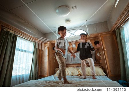 Joyful Kids Energetically Jumping on Bed in a Cozy Bedroom Setting 134393550