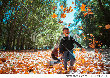 Children are Joyfully Playing and Laughing in Autumn Leaves at the Park 134393551