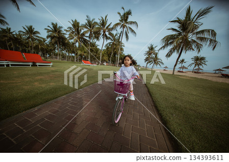 A child joyfully riding a pink bicycle on a scenic, sunny path A child joyfully riding a pink bicycle on a scenic, sunny path 134393611