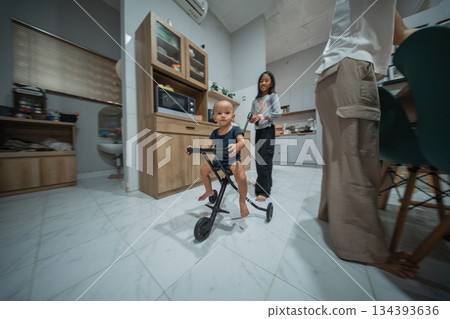 A joyful toddler happily riding a colorful tricycle in a modern kitchen 134393636
