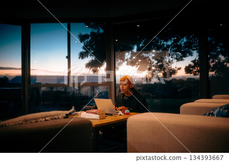 Young Professional Working Late into the Evening with a Stunning Sunset View in Sight Young Professional Working Late into the Evening with a Stunning Sunset View in Sight 134393667