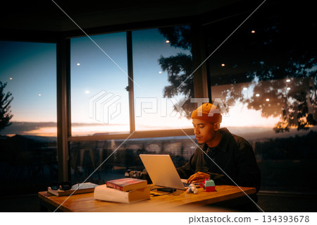 A Focused Young Individual Working Late Amidst a Scenic Sunset Sky 134393678