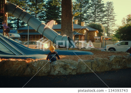 Child Playing by Slide in a Bright Sunlit Park with Trees and Cars Child Playing by Slide in a Bright Sunlit Park with Trees and Cars 134393743