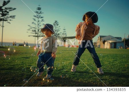 Joyful children are happily playing with colorful bubbles in a beautiful park setting Joyful children are happily playing with colorful bubbles in a beautiful park setting 134393835
