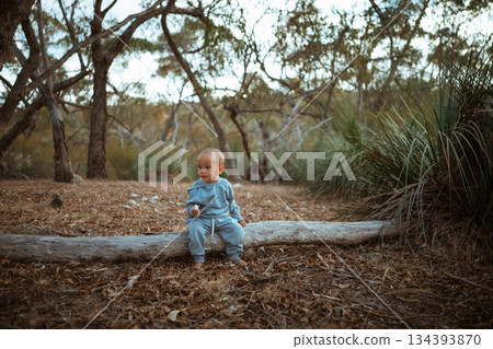 A young child happily sitting on a log in a beautiful natural landscape 134393870
