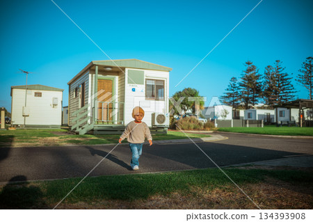 boy races between mobile homes, caucasian toddler in beanie dashes through sunny mobile 134393908