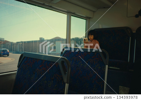 A passenger on public transport is gazing intently at their smartphone device, lost in thought 134393978