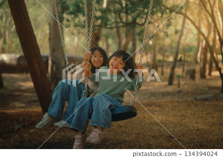 Having an enjoyable and joyful playtime on the swings in the vibrant, lush forested park area Having an enjoyable and joyful playtime on the swings in the vibrant, lush forested park area 134394024