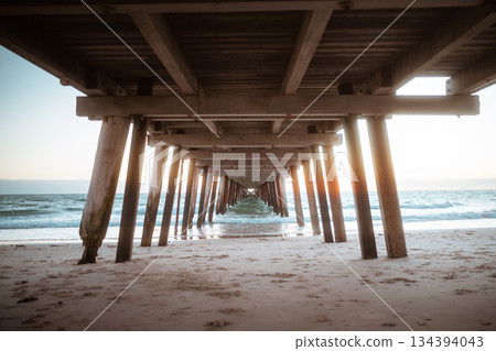 serene pier by sunrise, pier with wooden posts leading to glowing sunrise over ocean 134394043