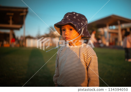 toddler in striped shirt and hat, closeup of toddler wearing hat in peaceful park setting 134394050