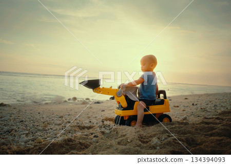 A Child Joyfully Playing on the Beach with a Colorful Toy Excavator at Sunset Time A Child Joyfully Playing on the Beach with a Colorful Toy Excavator at Sunset Time 134394093